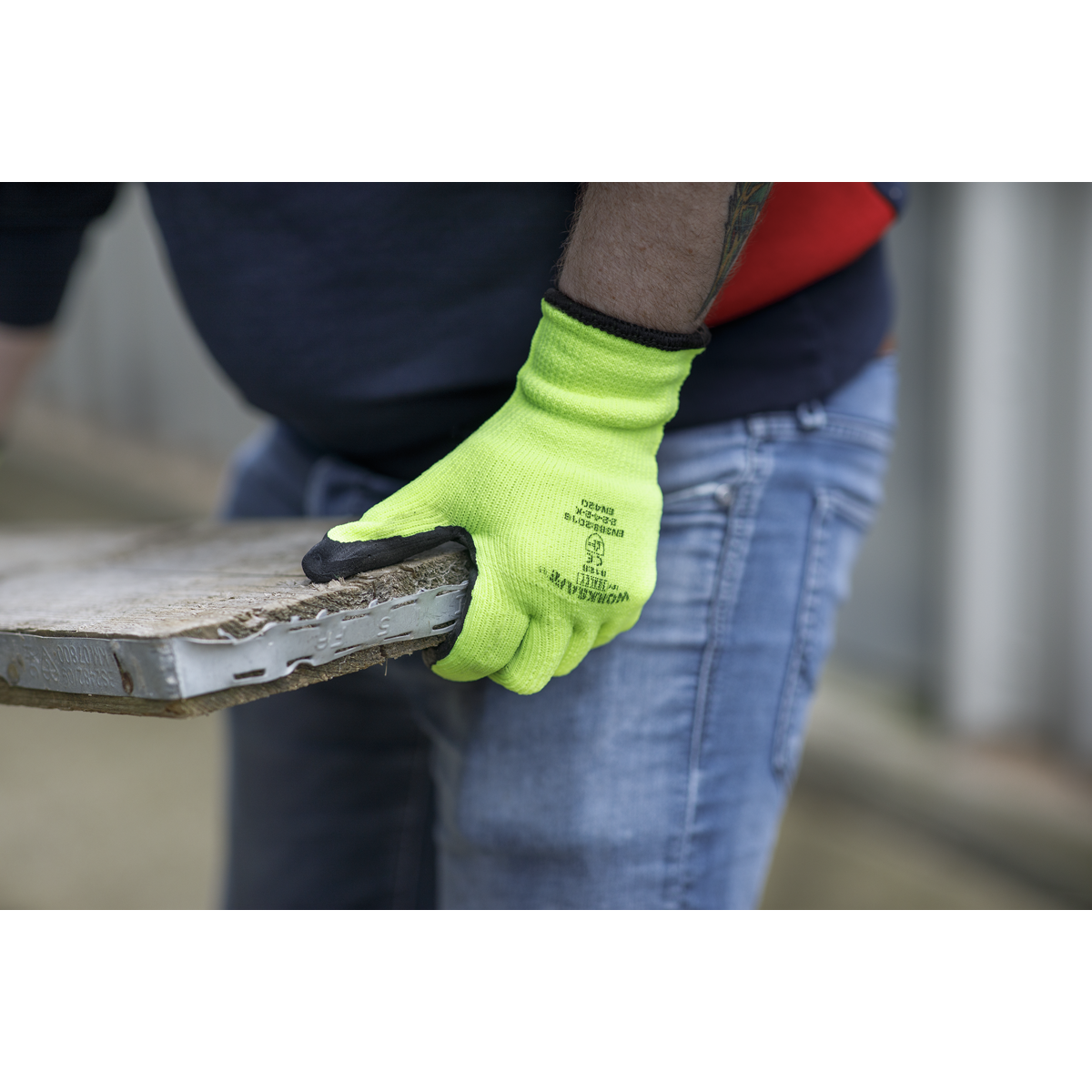 Person wearing a bright green glove holding a wooden pallet.
