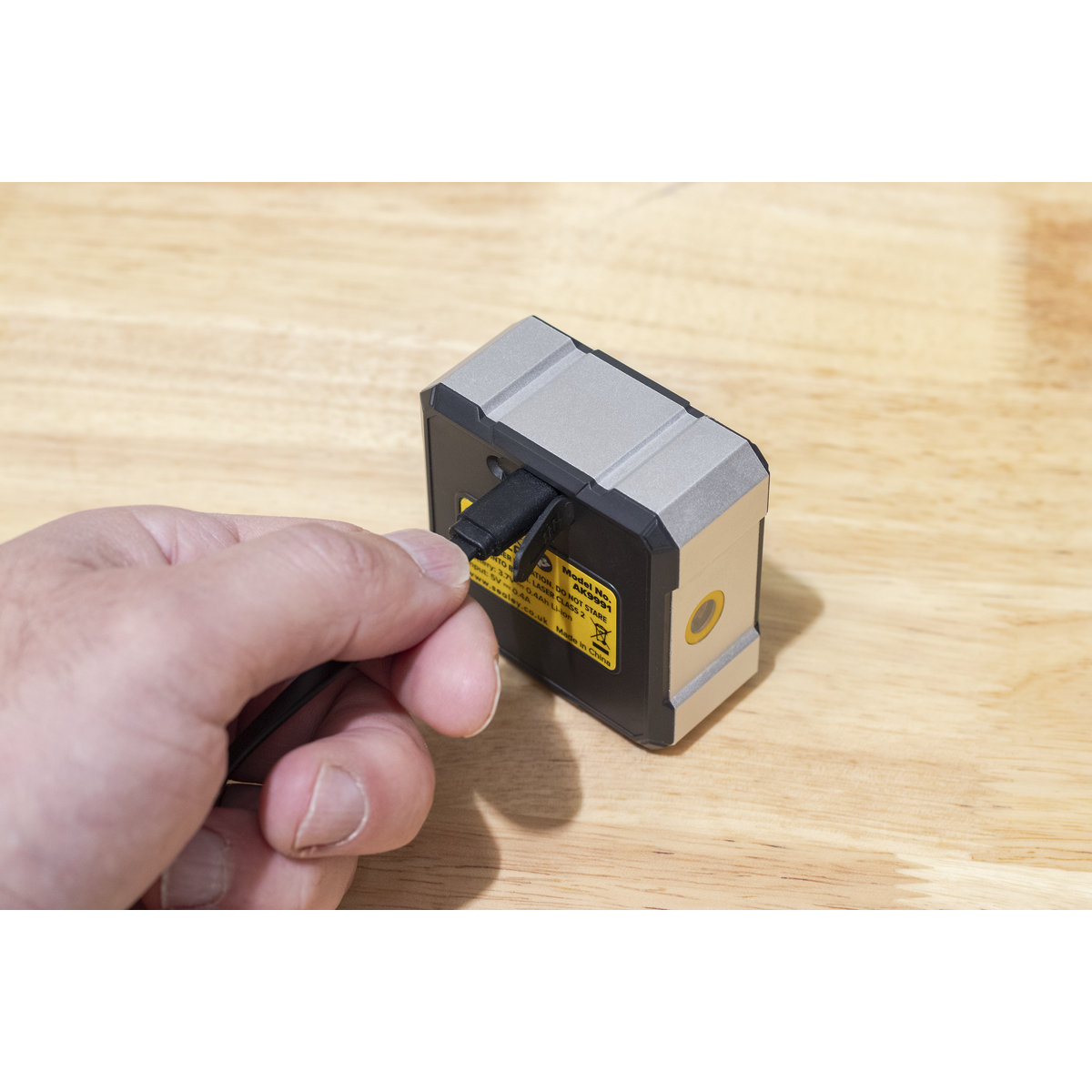 Hand holding a small electronic device on a wooden surface
